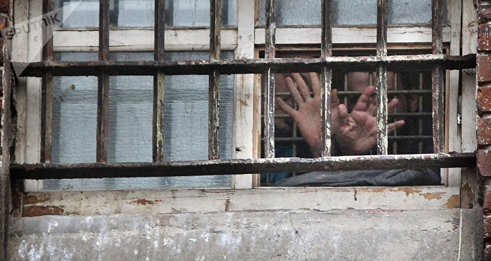 Заключенный протягивает руки сквозь решетку камеры в тюрьме